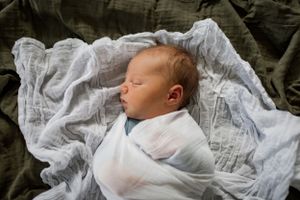 Peaceful newborn baby sleeping swaddled in white blanket.