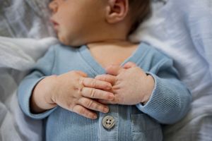 Close-up view of baby hands clasped together wearing a light blue cardigan sweater.