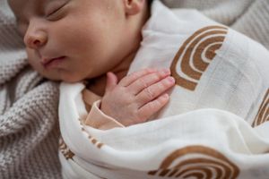 Close up of sleeping infant with tiny hands visible through rainbow patterned swaddle wrap.