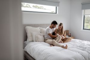 Modern bedroom interior with large window and comfortable white bedding.
