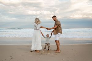 A family holds hands in a circle on the beach during golden hour.