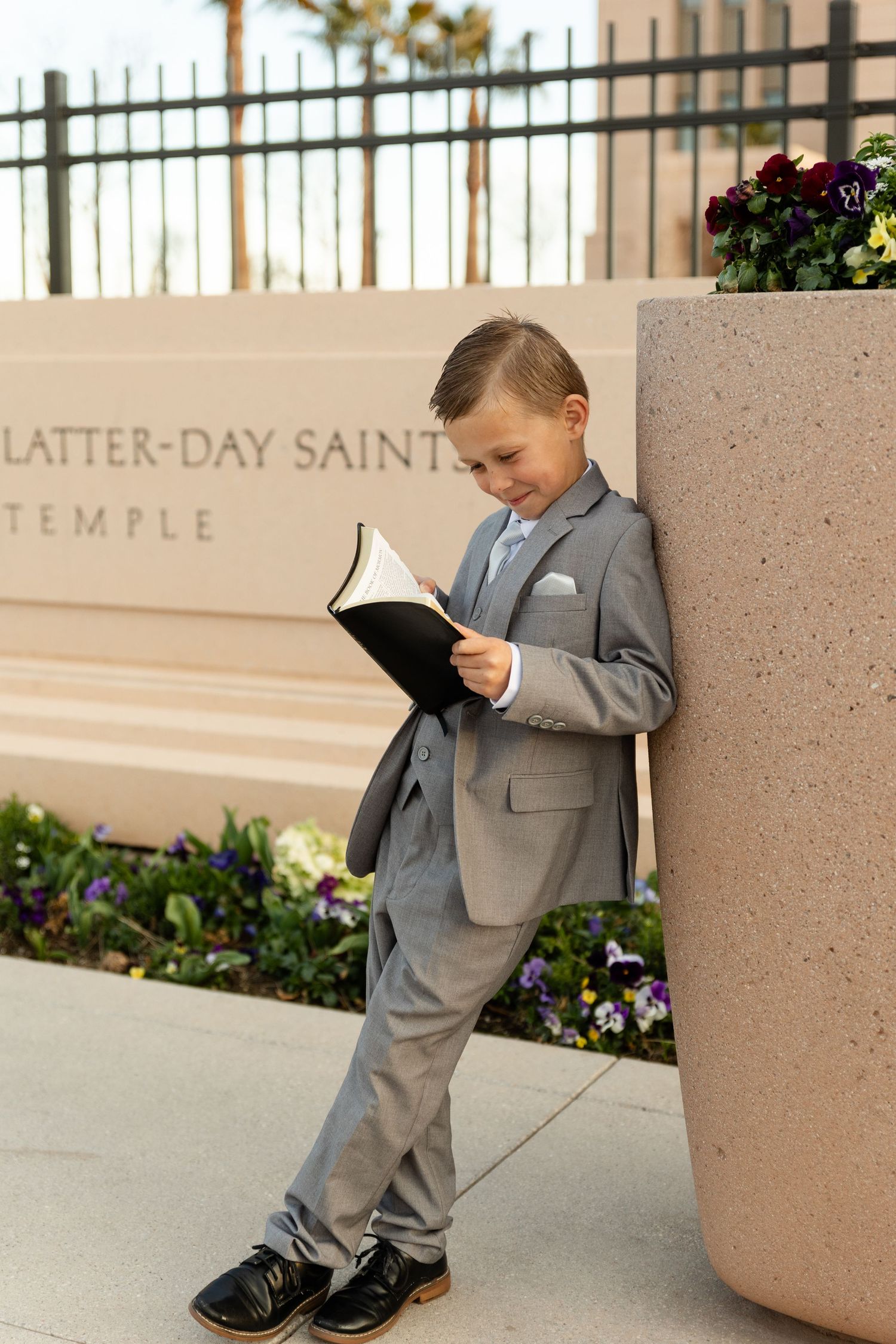 boy leaning on a planter reading his scriptures in his grey suit