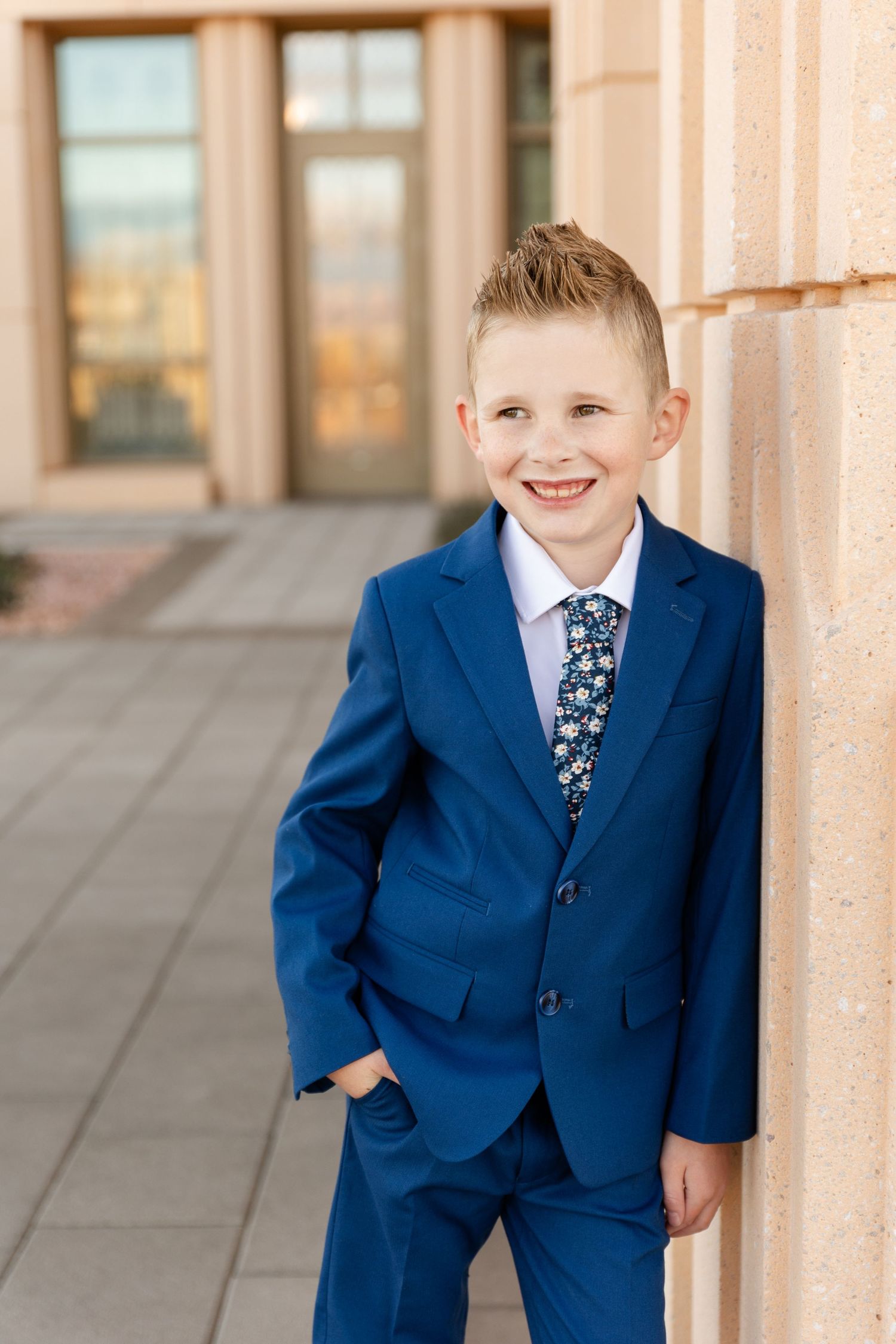 boy leaning on the pillar of a temple smiling off to the side in a blue suit