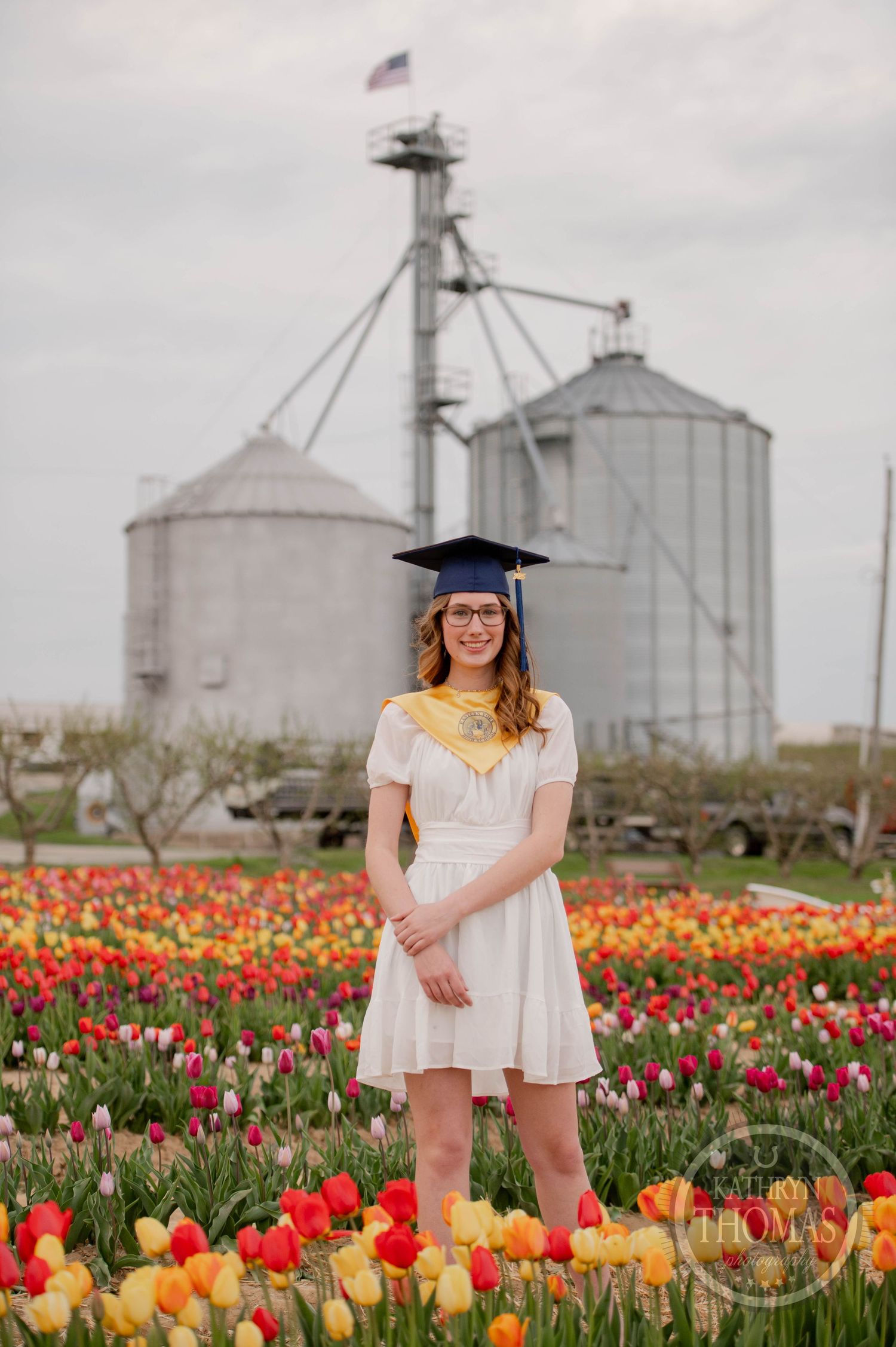 A graduation photo taken in front of farm grain silos with a colorful tulip field in full bloom.