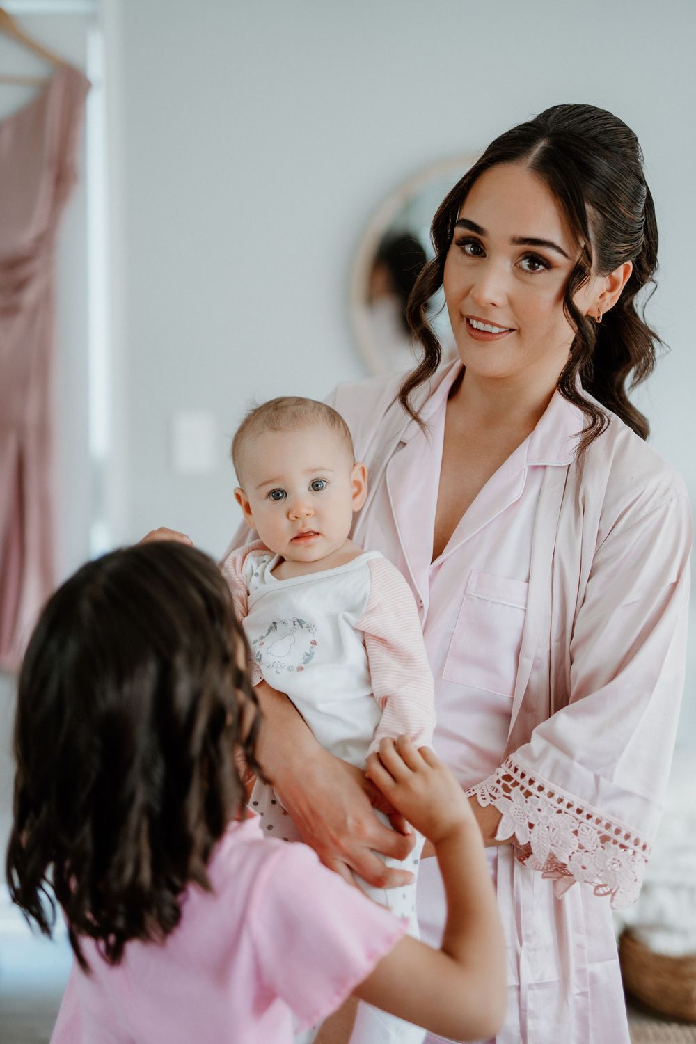A tender family moment as a small baby in white is held during what appears to be wedding preparations.