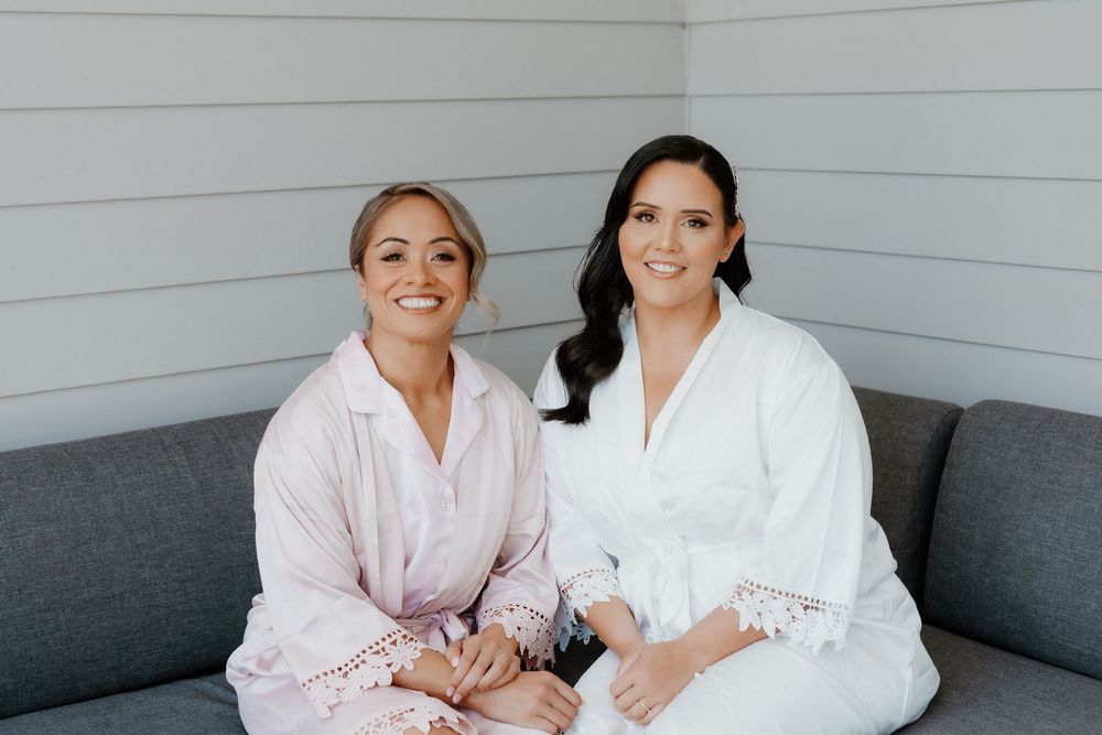Two people in cozy robes sitting together on a grey couch in a light-filled corner.
