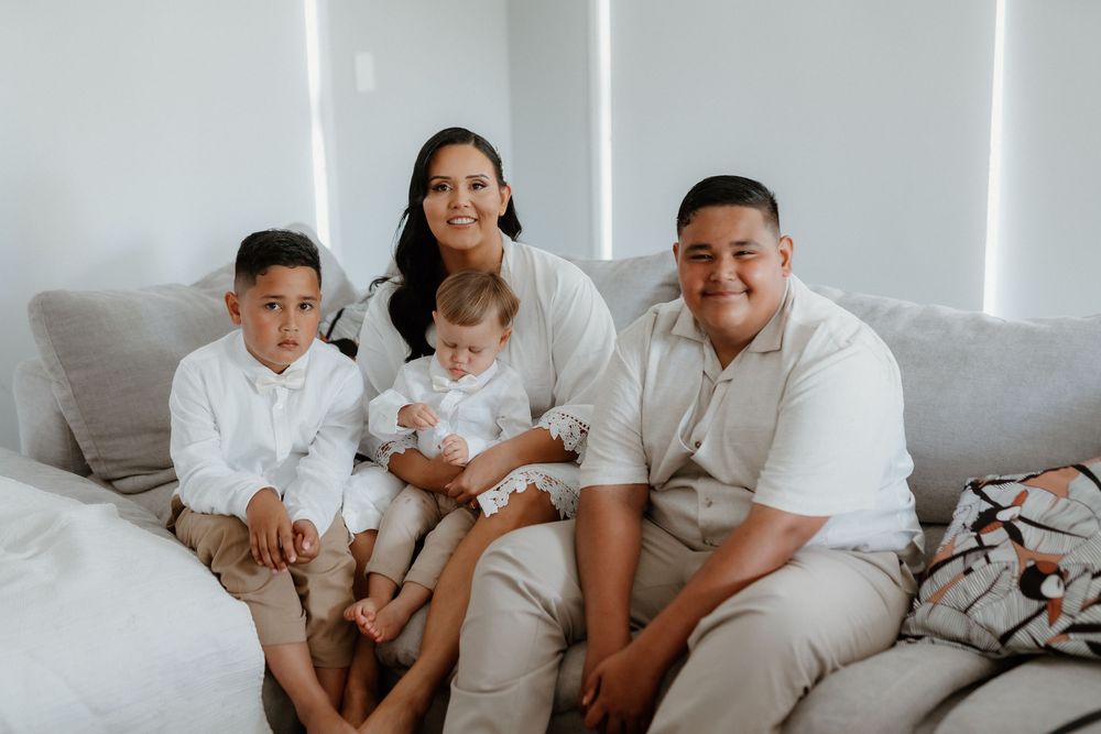 Family of four in white clothing sits together on a gray couch in a bright modern room.