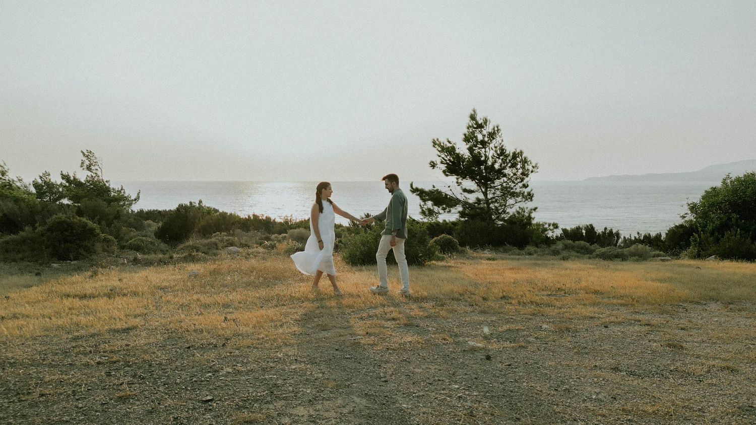 Two people dance together on a scenic hilltop overlooking a misty coastal landscape at sunset.