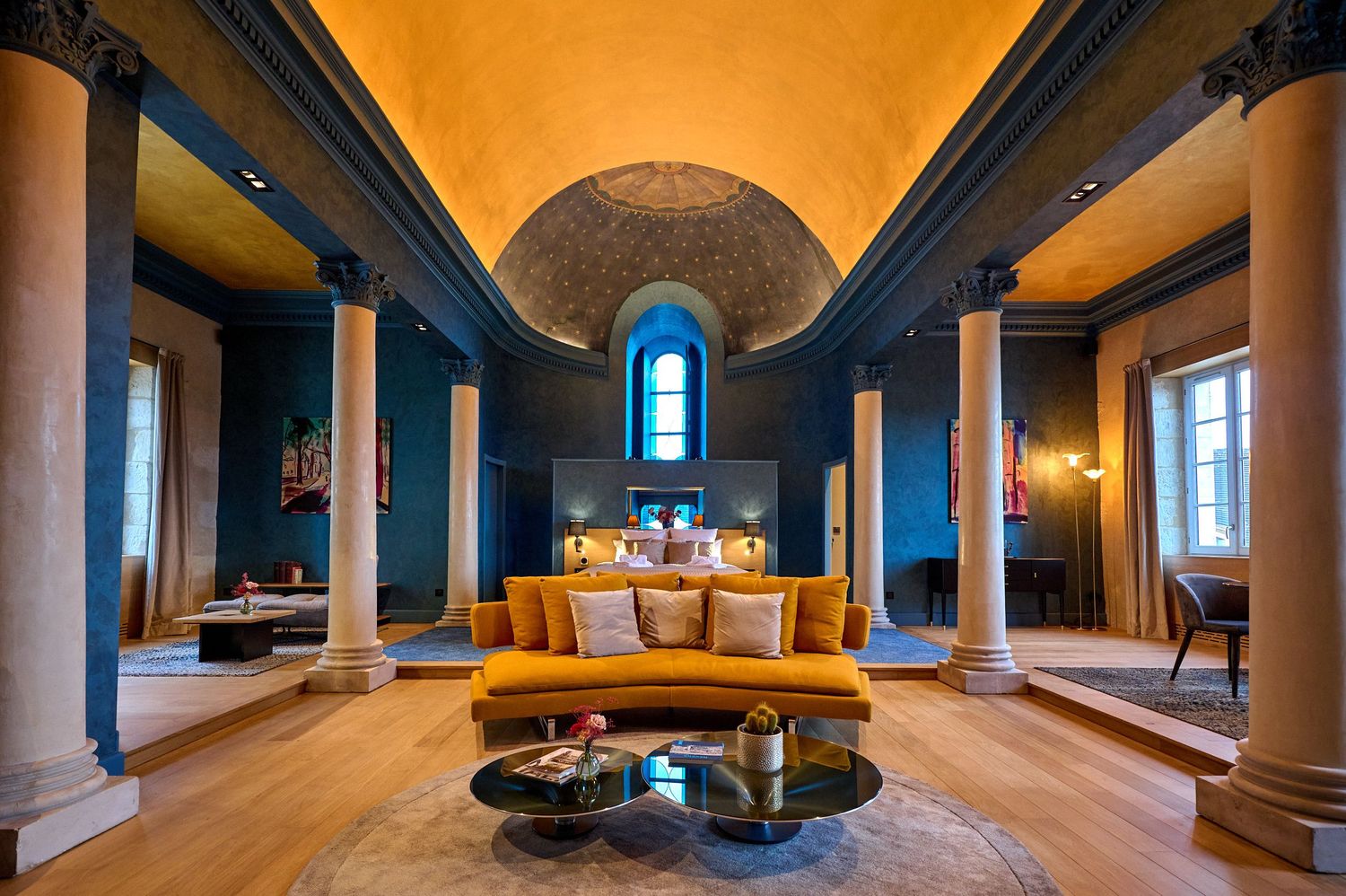 Panorama intérieur d'une chambre élégante avec plafond voûté, colonnes bleues et murs orange.