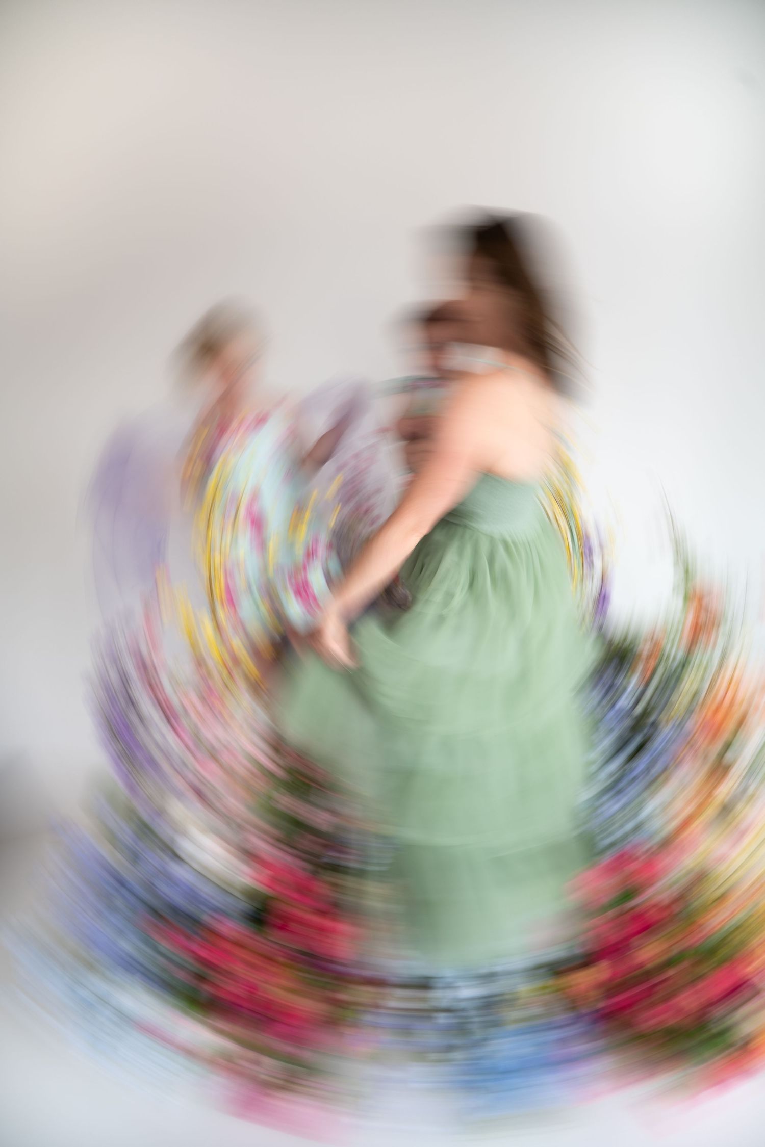 Blurred motion photo of figure in mint green dress twirling with colorful floral elements creating a spinning effect.