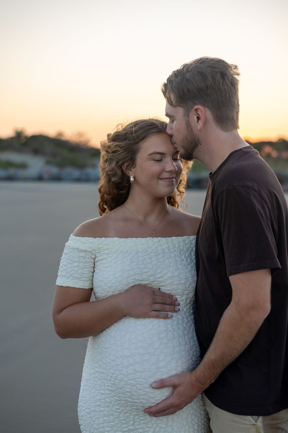 A couple shares intimate moments on a beach at sunset in a series of romantic maternity photos.