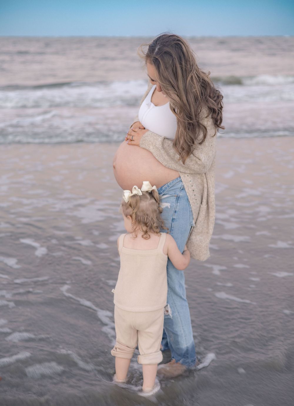 Two small children play together at the edge of the ocean waves on a sandy beach at sunset.