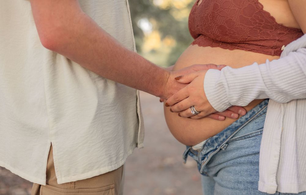 Close-up of hands cradling a pregnant belly in soft natural lighting outdoors.