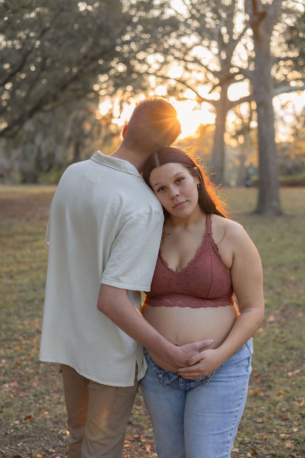 A couple embraces in a park at sunset with golden sunlight filtering through autumn trees.