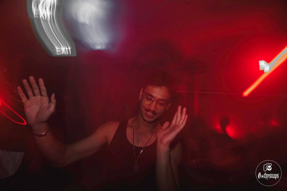 Silhouetted figure dancing with hands raised in dark nightclub with red lighting and motion blur effects.