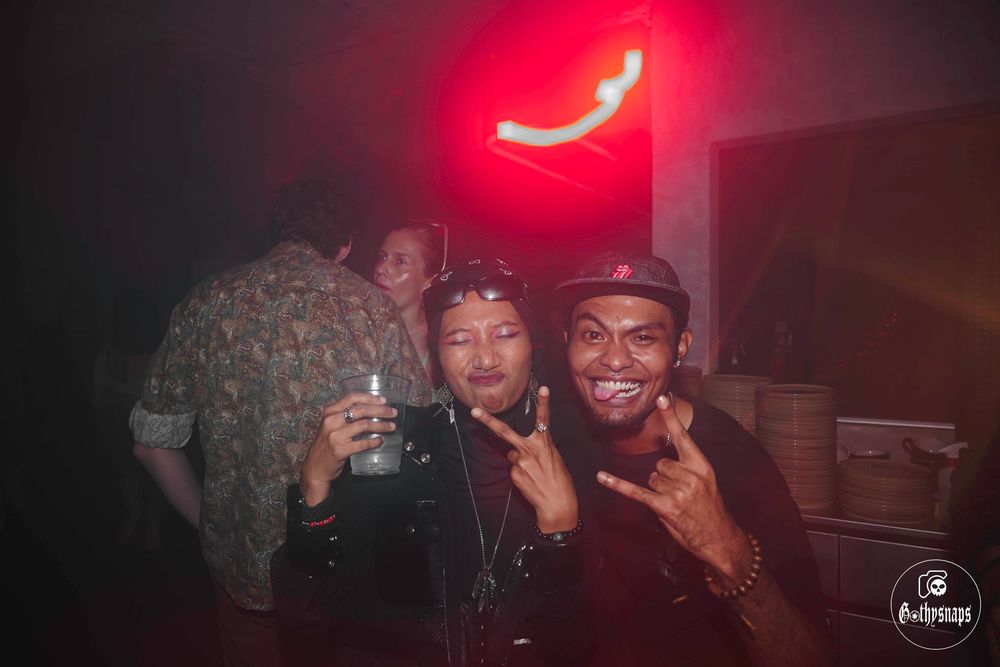 A group of friends pose together under a red neon light at a nightclub.