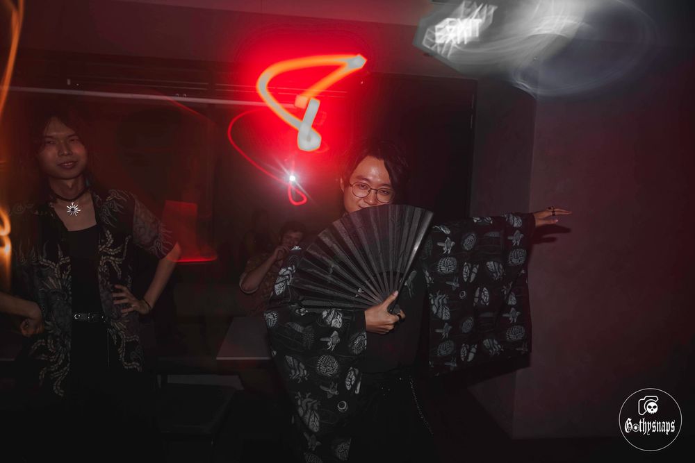 People dancing under a red neon light in a dark nightclub with fan props.