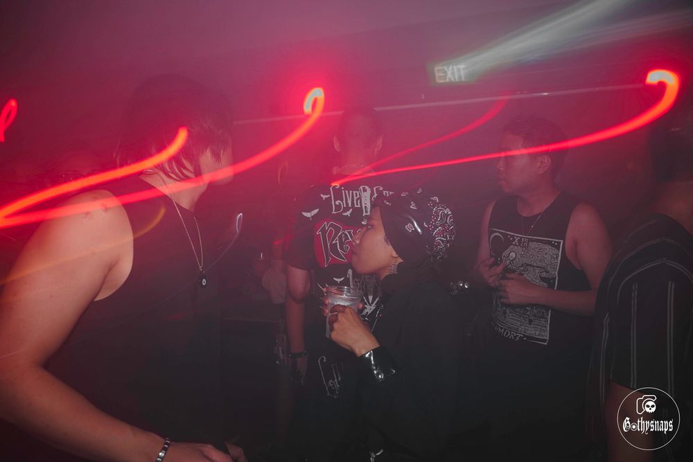 Red light trails create streaks across a dark nightclub scene with dancing silhouettes.