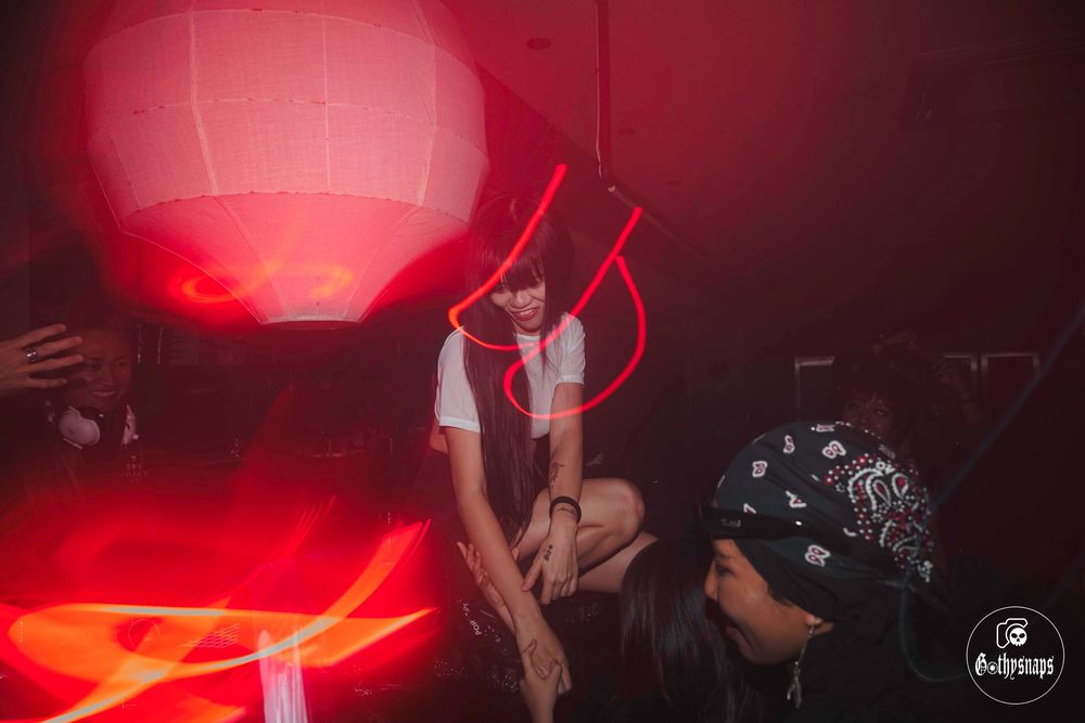 Silhouetted figures dance under a glowing red paper lantern at a nighttime party.