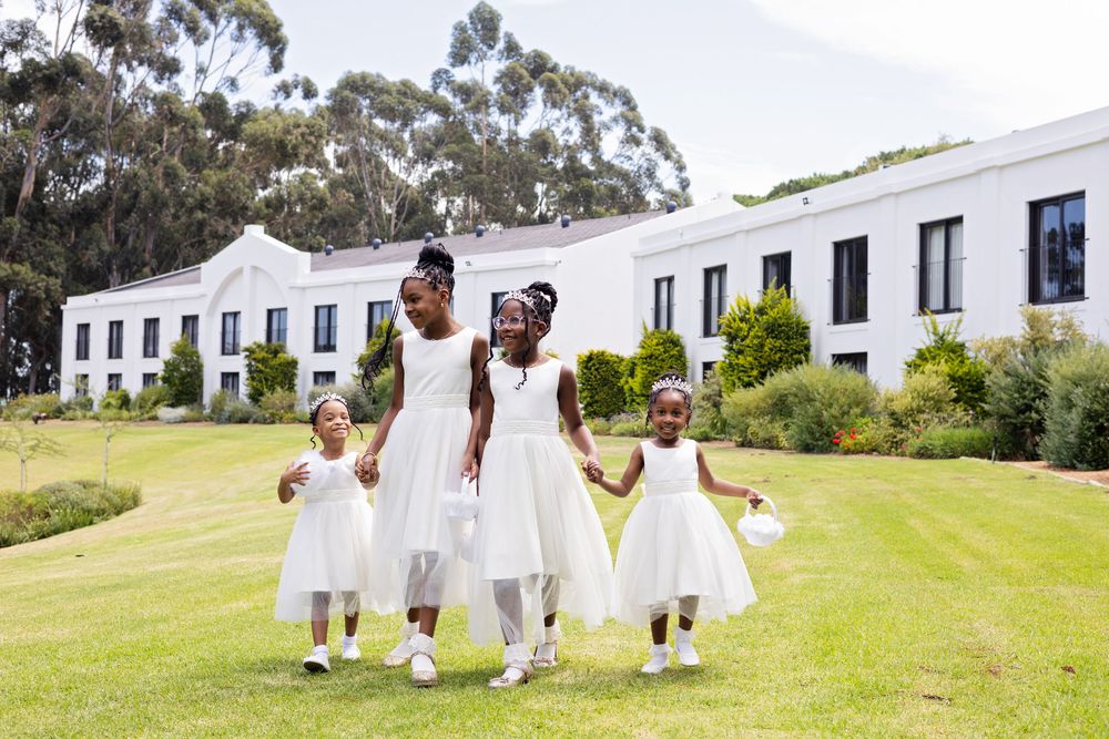 A group in white dresses walk together on a grassy lawn with white colonial-style buildings in the background.