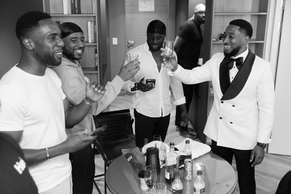 A group of people in formal attire laugh and socialize around a table with drinks at an indoor gathering.