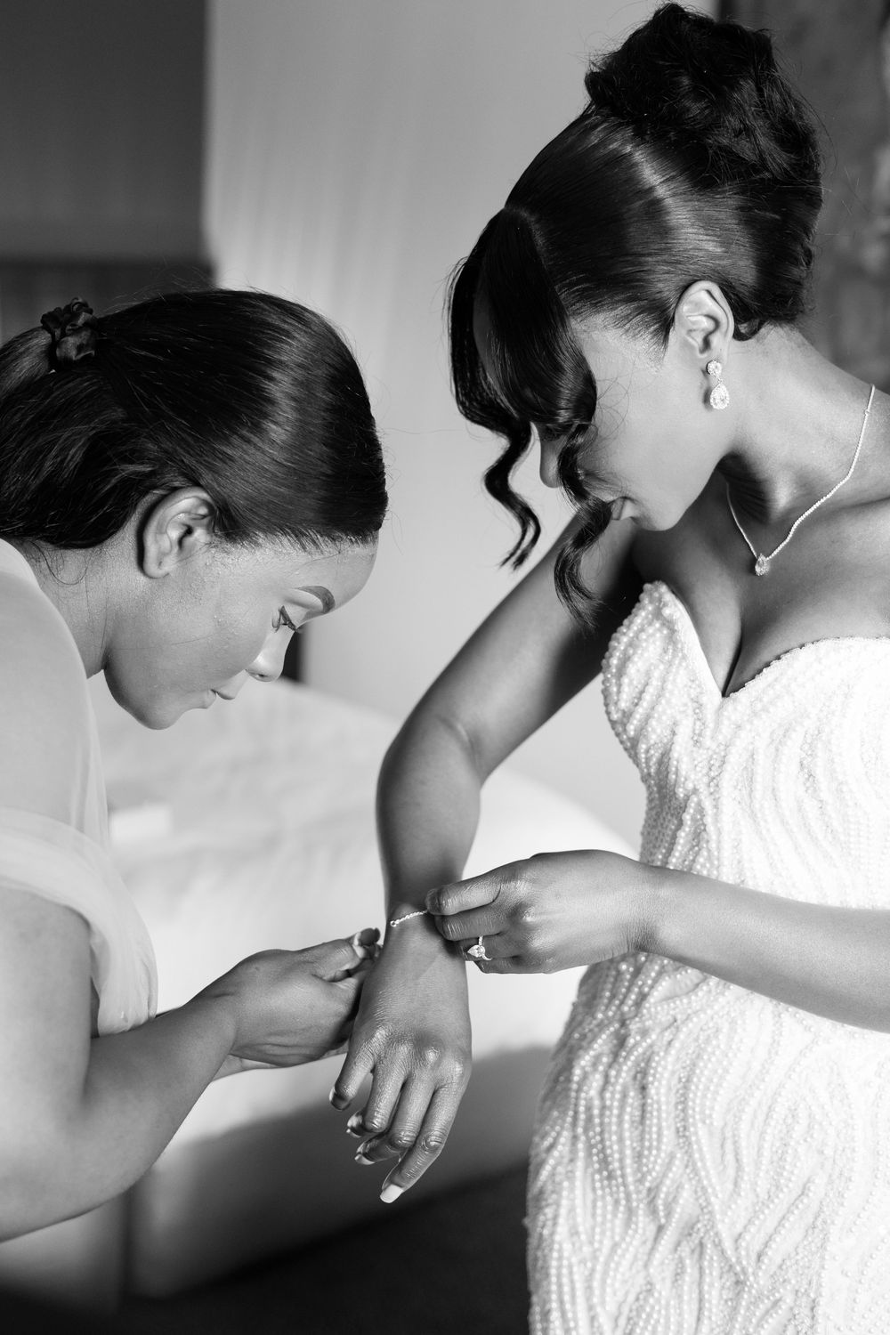 Two elegantly dressed figures share an intimate moment adjusting bridal jewelry before a wedding ceremony.