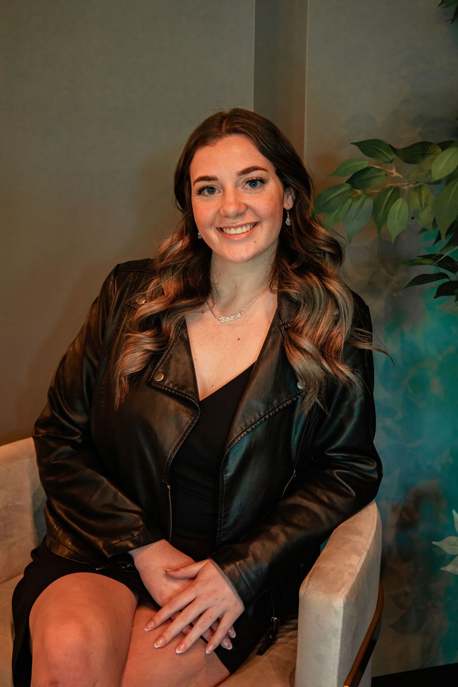 Professional portrait of woman in leather jacket seated in elegant setting.