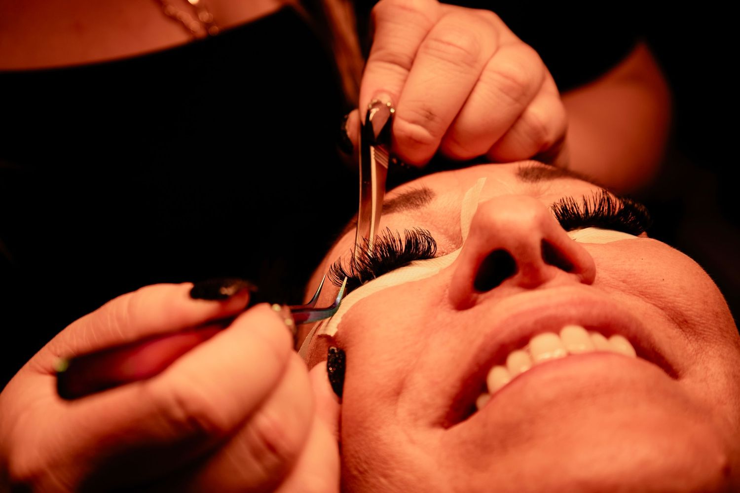 Dark and moody close-up shot showing lash extension application in warm lighting.