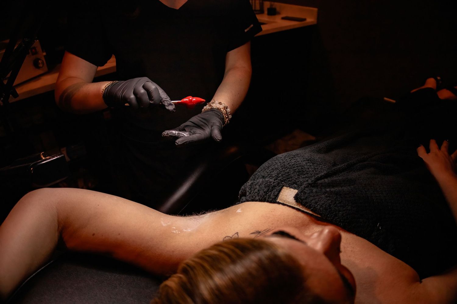 Professional beauty technician applying individual eyelash extensions in dramatic lighting.