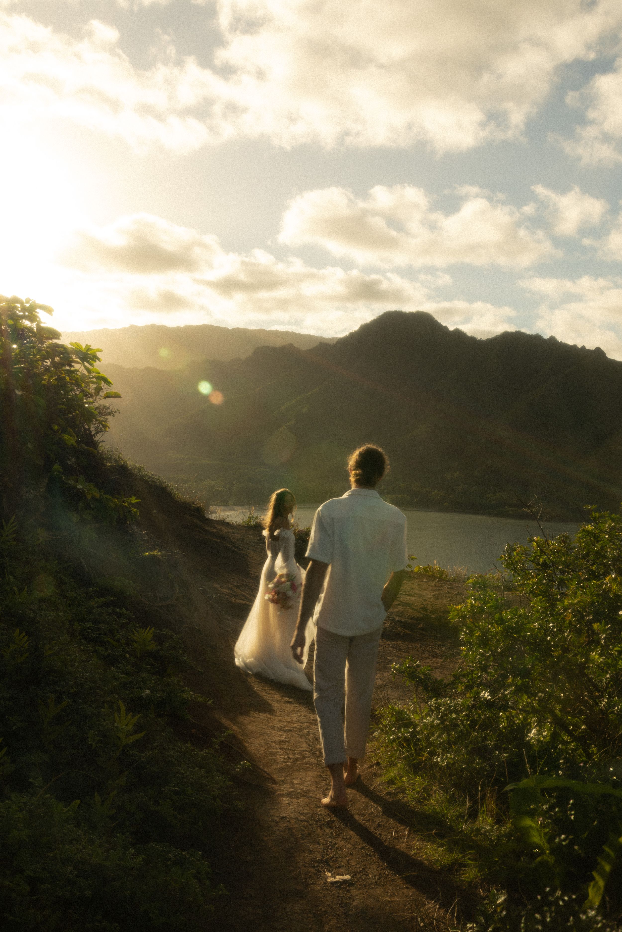 A couple walks along a mountain trail at sunset overlooking a scenic lake view.