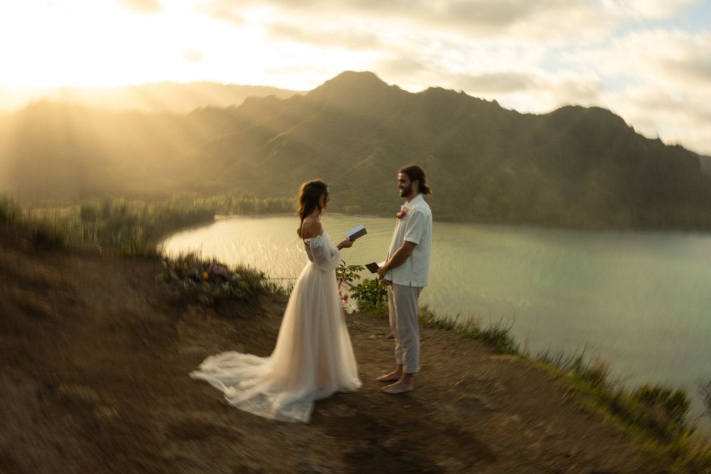 Wedding couple stands on mountain overlook during golden sunset beside a serene lake.