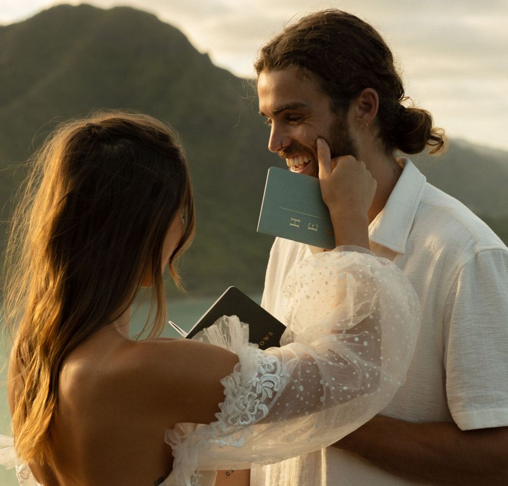 A couple shares a tender moment at sunset on a mountaintop, with the bride wearing a delicate lace dress.