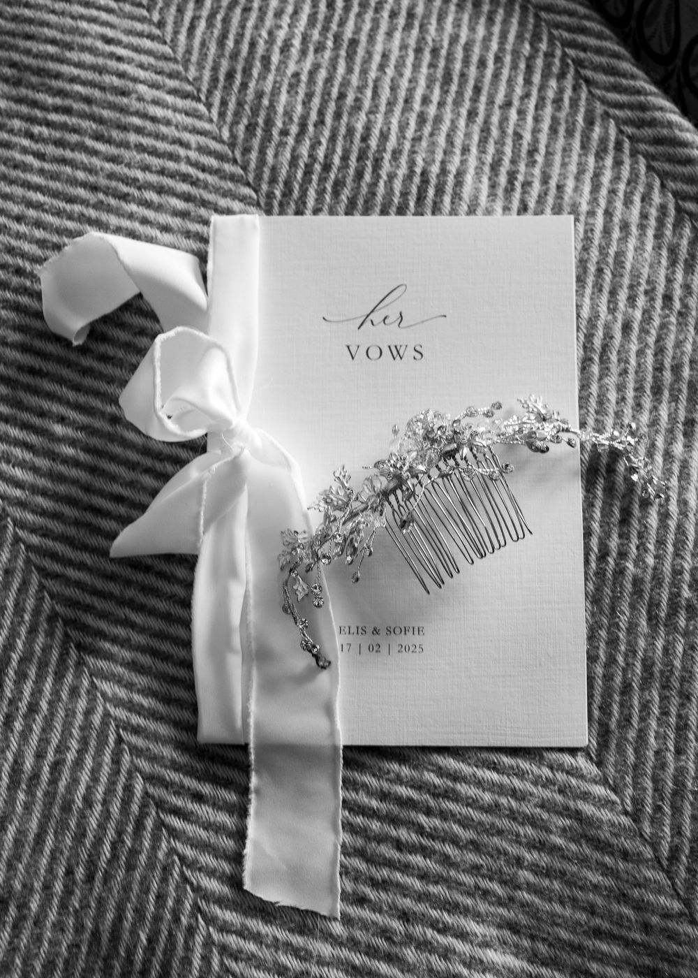 Wedding vows booklet with ornate hair accessories and white ribbon on grey textile.