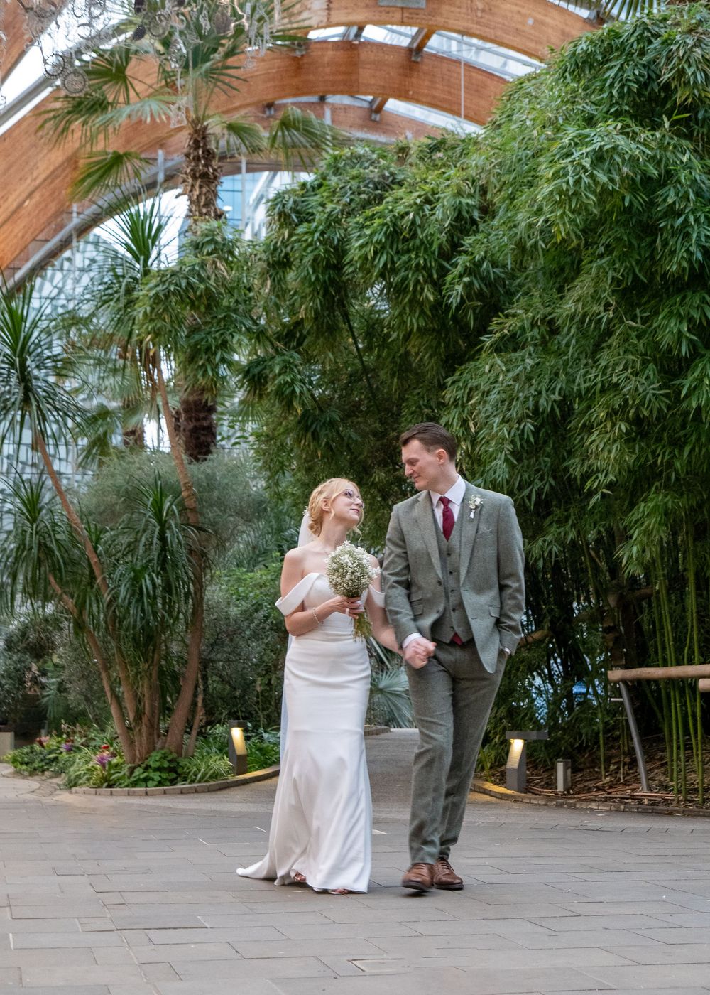 Sheffield Town Hall Wedding - Newlyweds walking hand in hand through a lush indoor peace garden sheffield with palm trees.