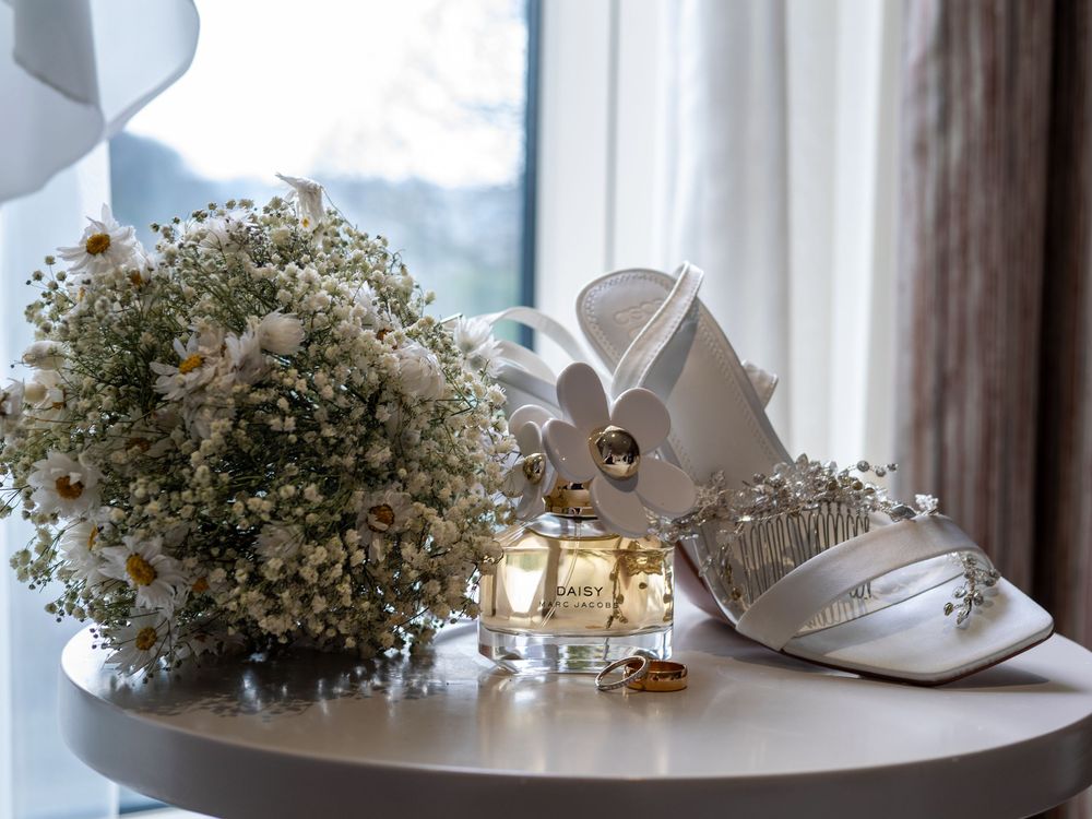Sheffield Town Hall Wedding - Wedding accessories including white shoes, baby's breath flowers and perfume on a round table.