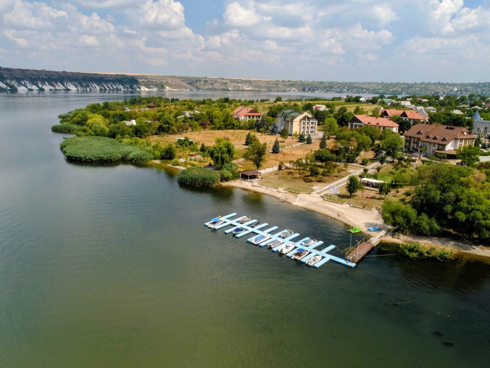 Aerial view of a riverside resort with a boat dock, lush trees, and buildings along a calm river.