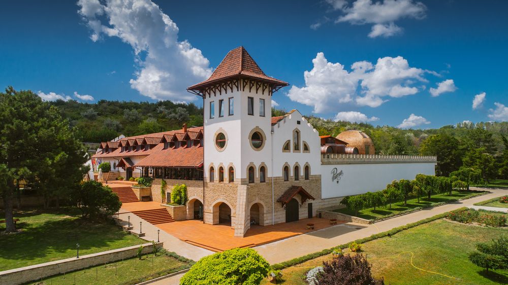 Aerial view of a white Mediterranean-style winery building surrounded by lush green trees and gardens.