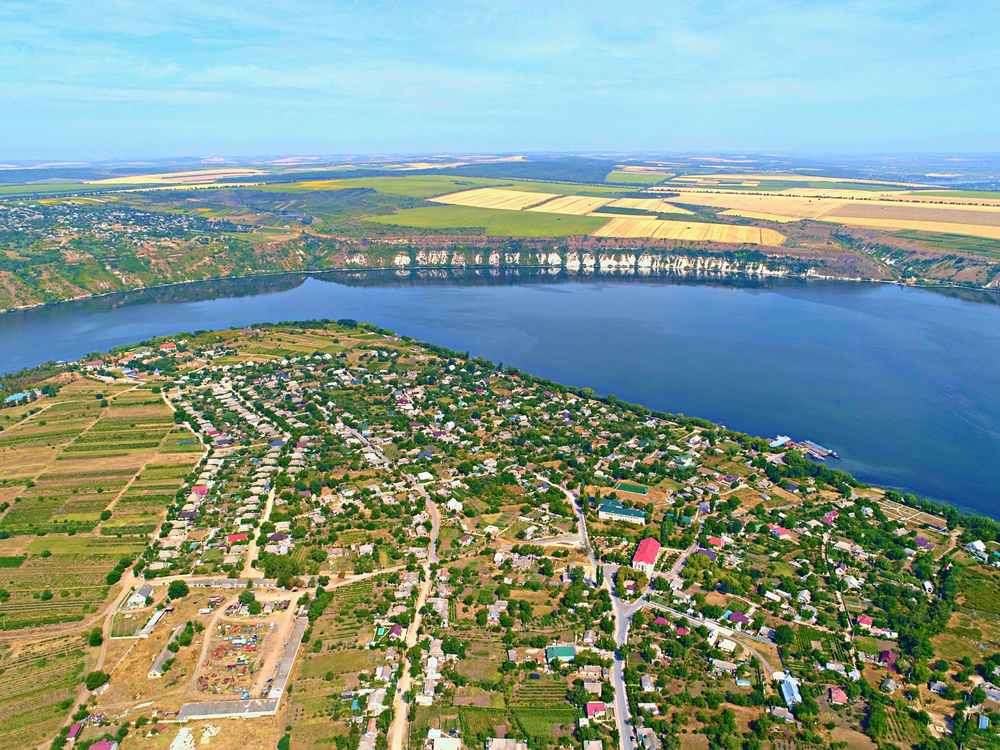 Aerial view of a small village nestled between agricultural fields and a large river reservoir.
