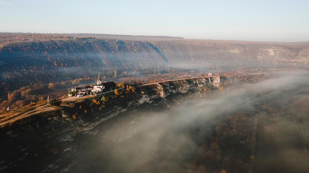 Aerial view of a misty canyon with fog rolling over dramatic cliffs at sunrise.