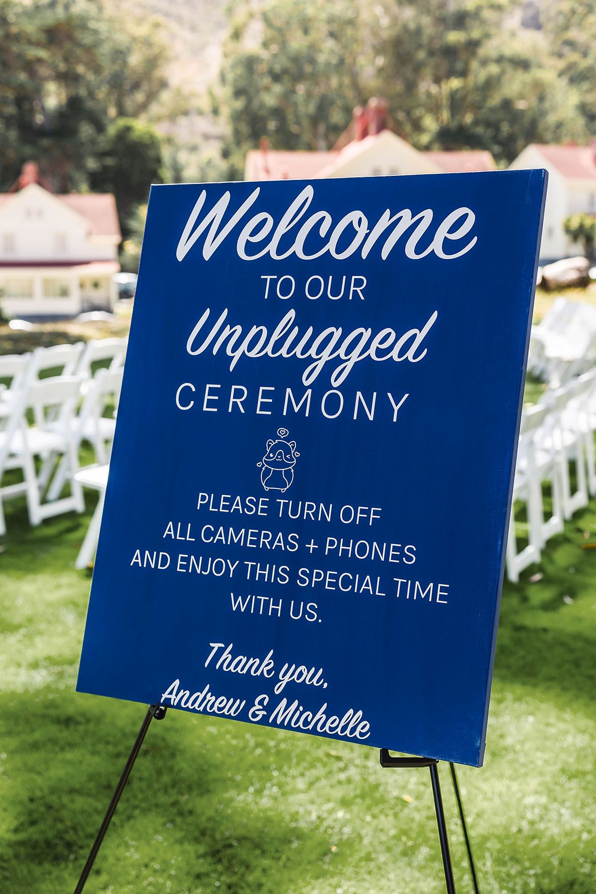 An outdoor wedding ceremony setup with white chairs on green lawn, overlooking historic buildings and mountains in background.