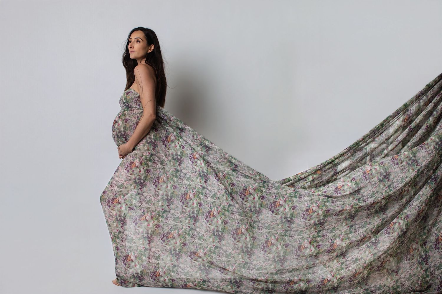 Black and white artistic maternity photo showing a woman cradling her pregnant belly in a flowing white shirt.