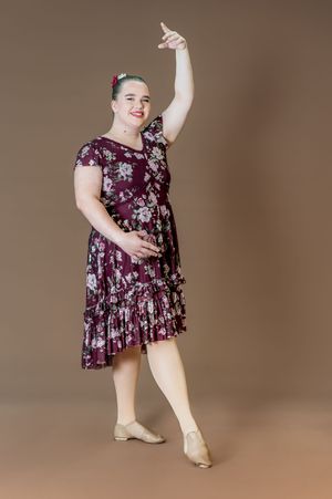 Dancer poses gracefully in floral burgundy dress against brown backdrop.