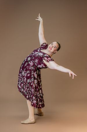 Dancer in flowing burgundy floral dress performs expressive dance move.