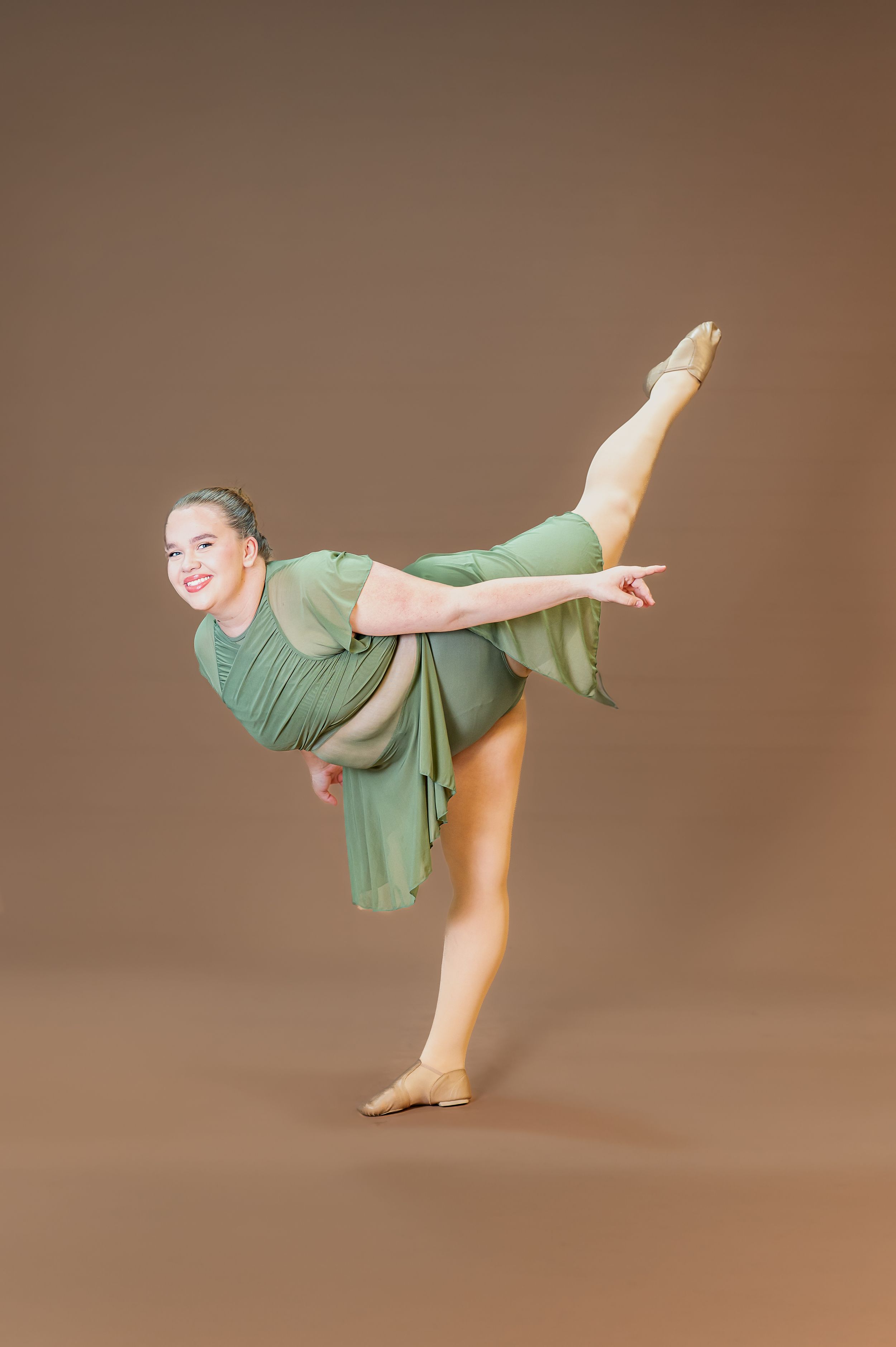 Dancer in sage green outfit performs arabesque pose with pointed toes.