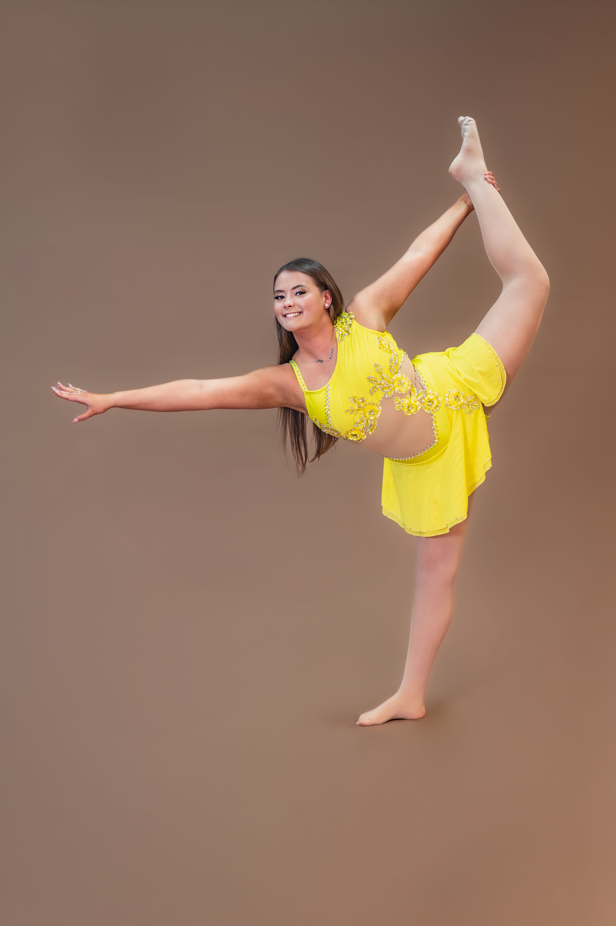 Dancer in yellow costume demonstrates impressive flexibility with standing split pose.