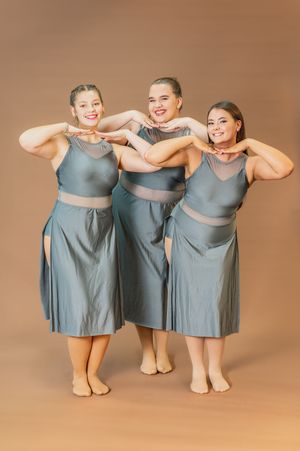 Three dancers in matching grey outfits perform synchronized pose.