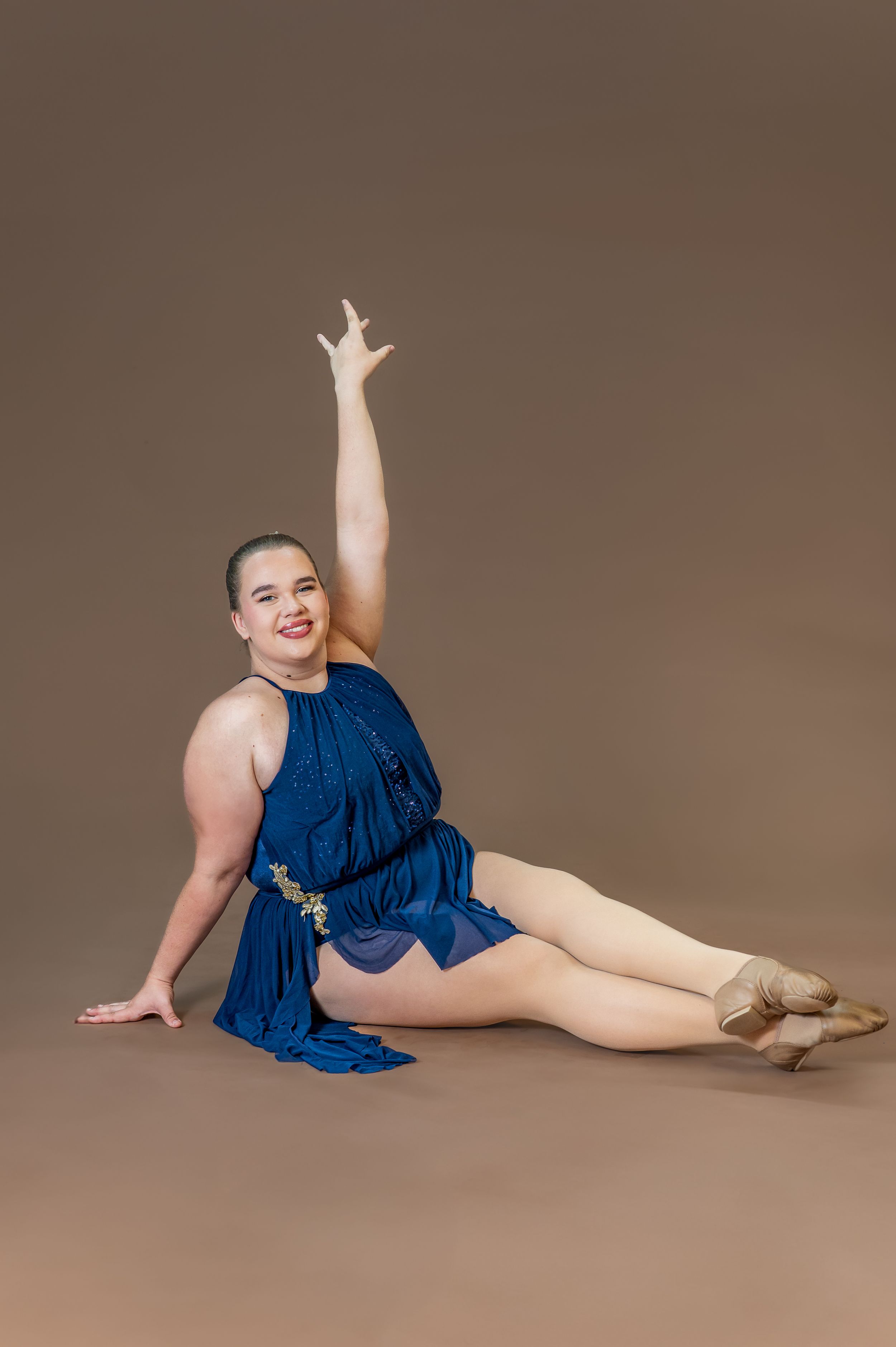 Dancer in navy blue dress performs seated pose with raised arm.
