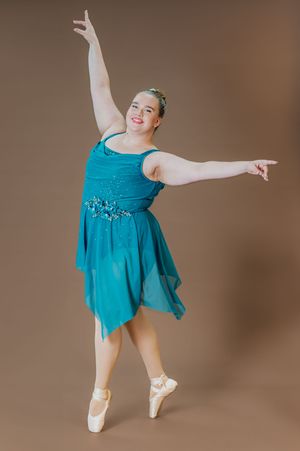 Dancer in turquoise sequined dress performs graceful ballet pose on pointe.