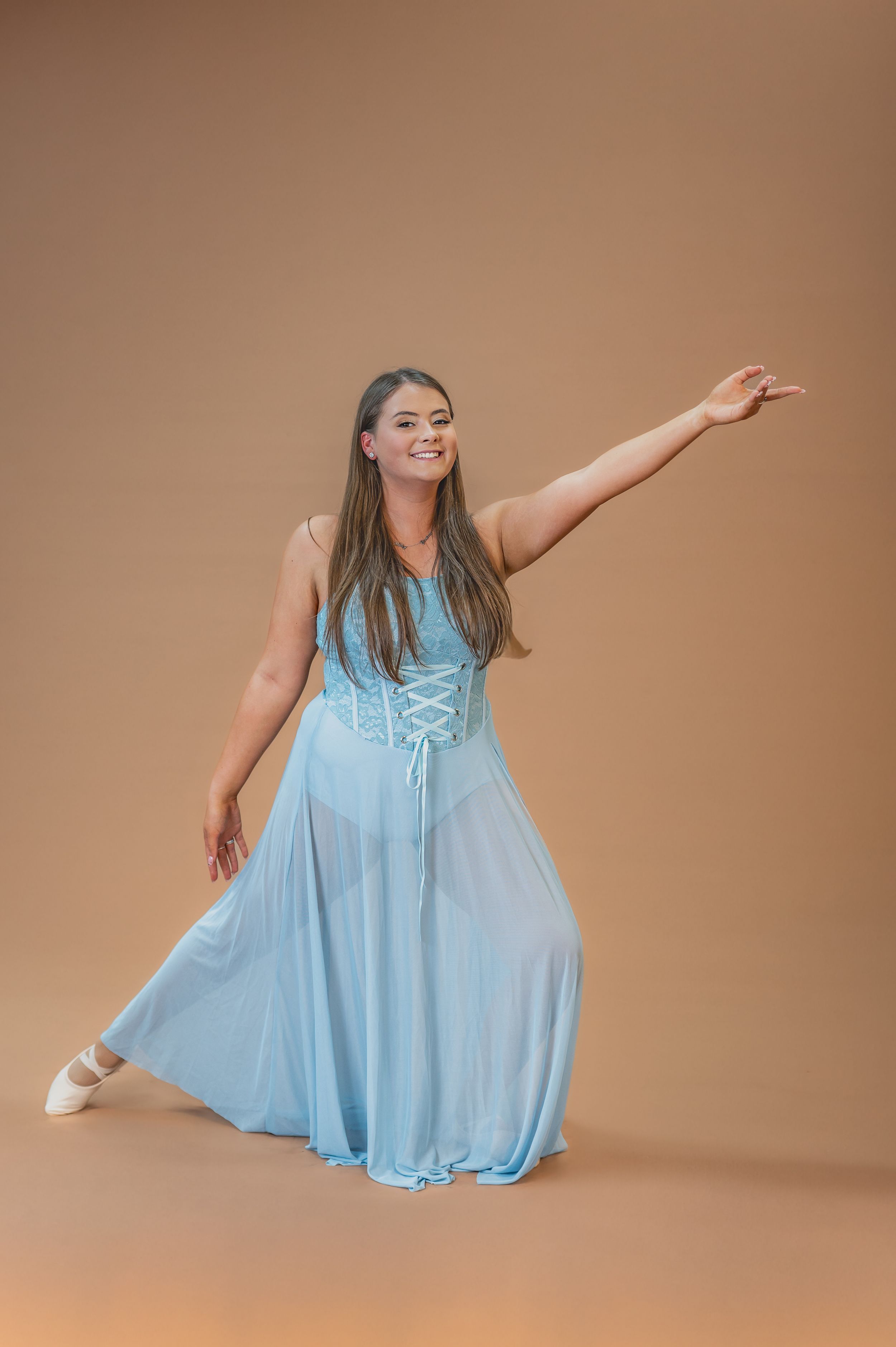 Dancer in flowing light blue dress performs graceful pose against brown backdrop.