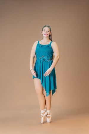 Ballet dancer in teal dress poses en pointe with elegant arm positioning.